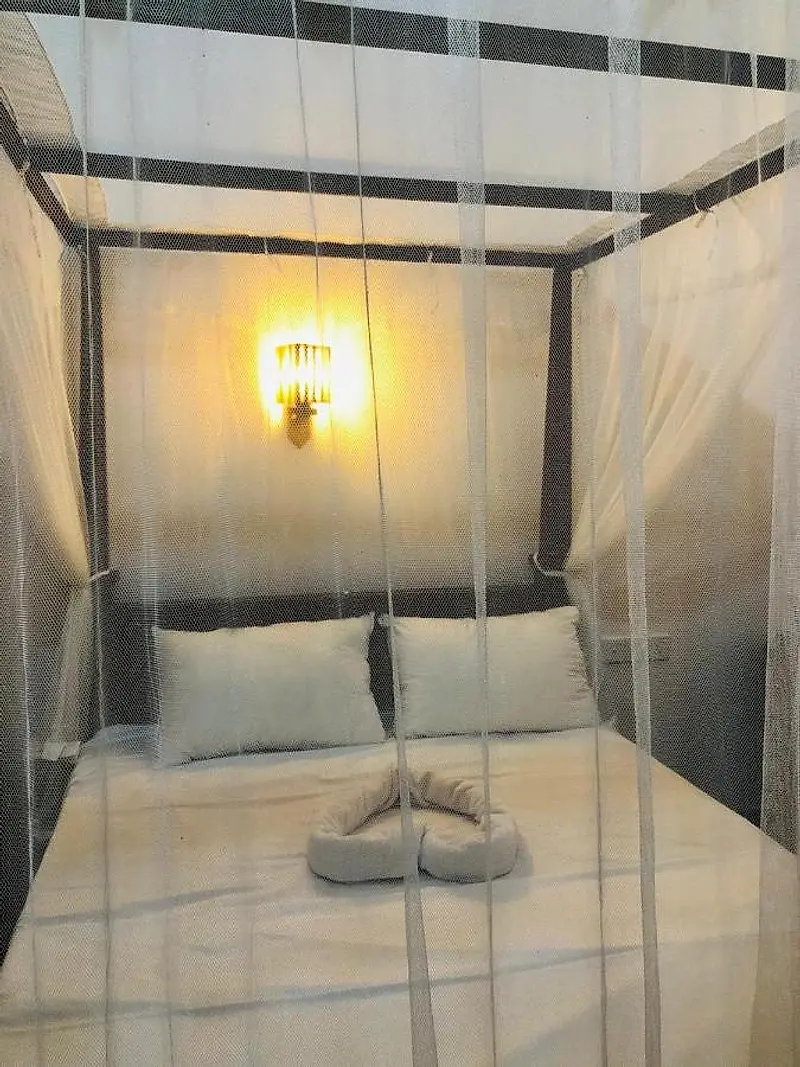 Four-poster double bed with the mosquito net drawn, under a warm wall lamp