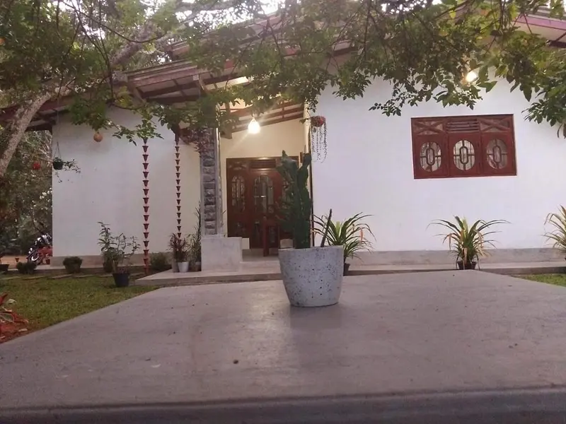 The white single-storey guest house with its teak doors, red veranda pillars and potted palms around the courtyard